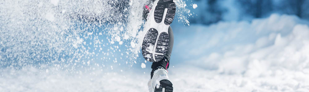 Close-up of person's feet running through the snow with snow spraying up around them